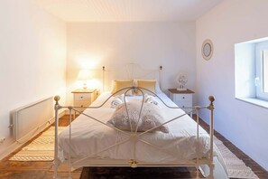 Ein Bett mit Metallgestell, ein Nachttisch mit Lampe sowie ein an der Wand befestigter Spiegel.