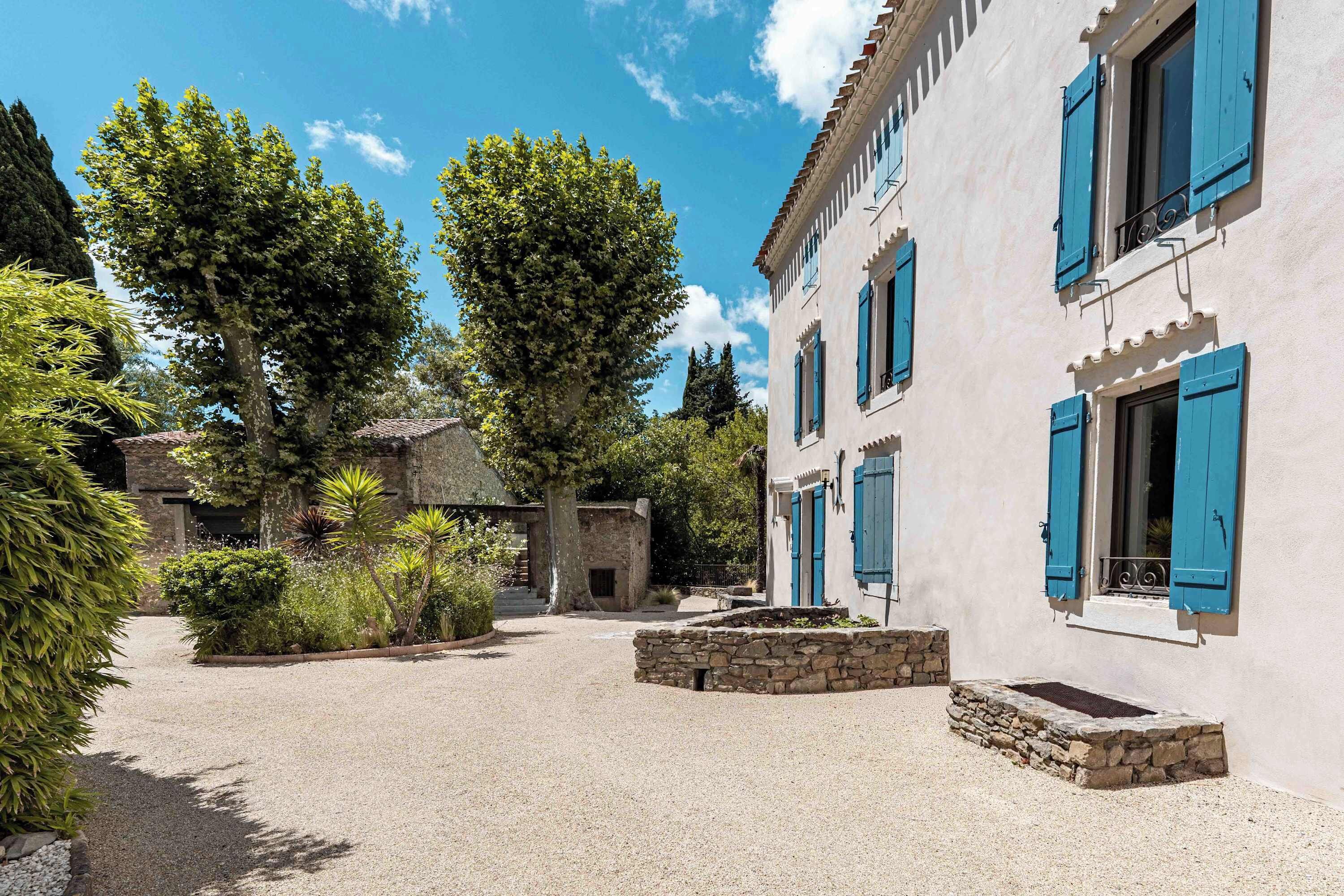 A courtyard with a gravel path, stone walls, and a building with blue shutters.