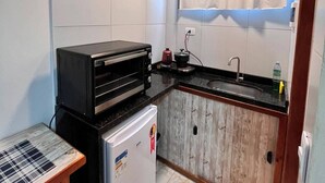 Eine kleine Küche mit weißen Fliesen, einem schwarzen Toaster, einem kleinen Kühlschrank und einem Holzschrank.