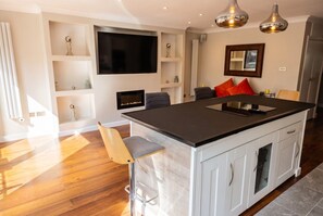A modern kitchen with a central island, bar stools, a flat-screen TV, and pendant lighting. - Top-Floor 3-Bed Flat Sleeps 6 · Free Parking · Walk to Clissold Park (Greater London)