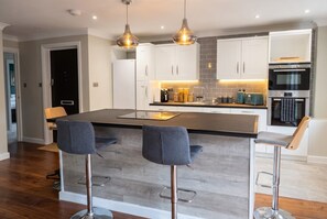 A modern kitchen with a central island, bar stools, pendant lighting, and stainless steel appliances. - Top-Floor 3-Bed Flat Sleeps 6 · Free Parking · Walk to Clissold Park (Greater London)