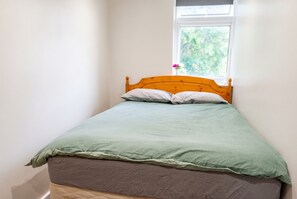 Un lit simple avec une tête de lit en bois, une couvre-lit verte et une fenêtre donnant sur un paysage verdoyant.