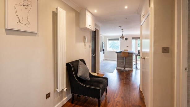 A hallway with a black chair, a radiator, and a kitchen area in the distance. - Top-Floor 3-Bed Flat Sleeps 6 · Free Parking · Walk to Clissold Park (Greater London)