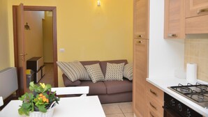 A compact kitchen with a stove, cabinets, and a dining area with a table and a couch. - Apartment 'Rietinn - Loggia Del Vignola' with Wi-Fi (Rieti)