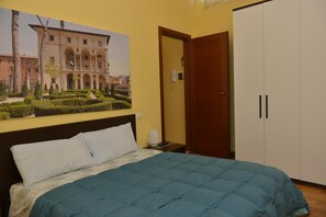 Una habitación de hotel con cama, mesita de noche, lámpara, armario y un cartel grande en la pared.
