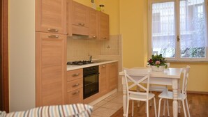 A compact kitchen with wooden cabinets, a gas stove, an oven, and a dining area with a table and chairs. - Apartment 'Rietinn - Loggia Del Vignola' with Wi-Fi (Rieti)