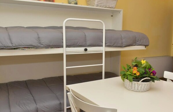 Una cama litera con escalera, una mesa y una cesta de flores.