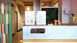 A reception desk with a marble top, a sign reading 'RECEPTION', and a green wall with a floral arrangement behind it.