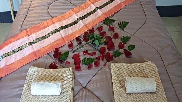 Una cama con un cabecero decorativo, dos toallas blancas y pétalos de rosa esparcidos.