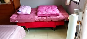 A room with a red bed, two pink pillows, a white bedside table, and a white lamp.