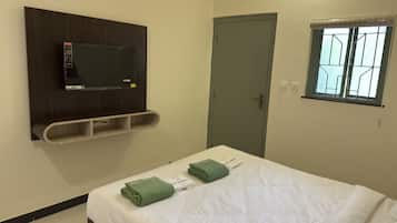 A hotel room with a bed, a TV mounted on the wall, a door, and a window.