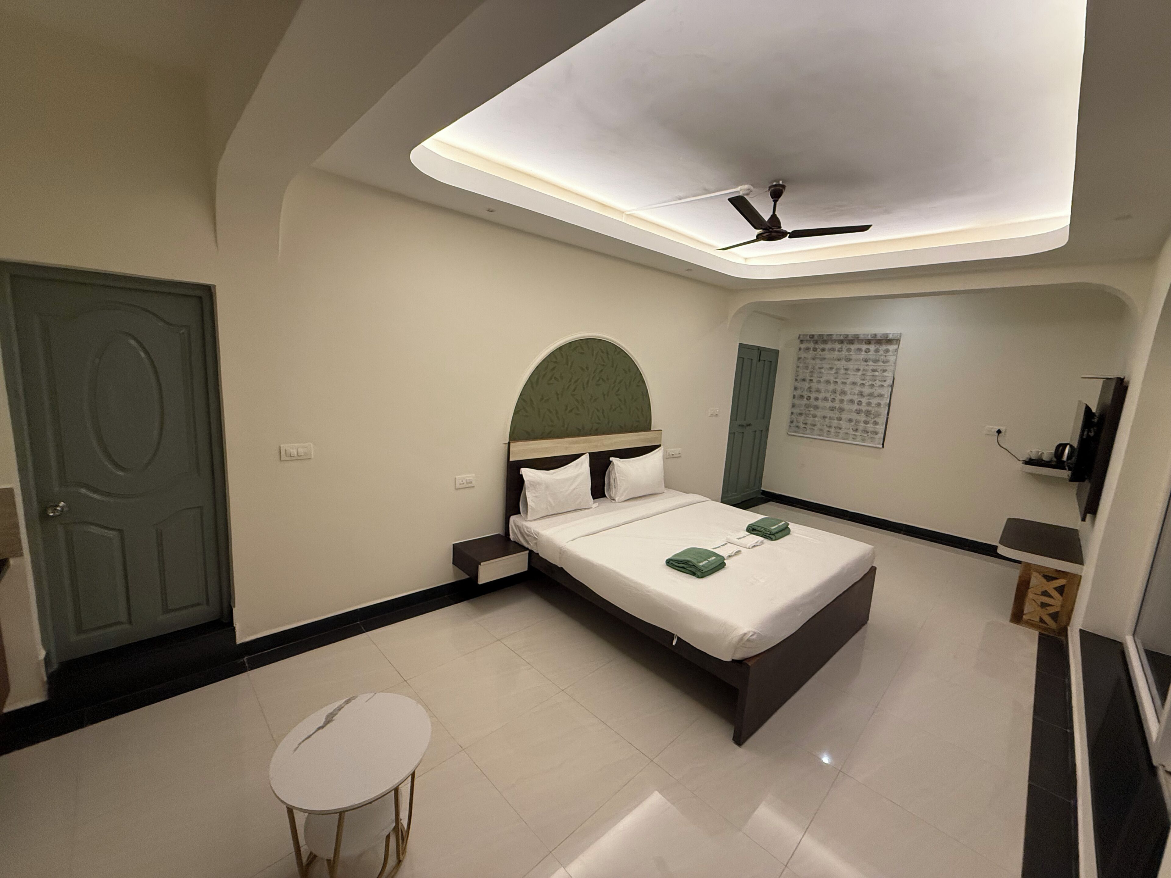 A hotel room with a bed, a ceiling fan, a small table, and a door.