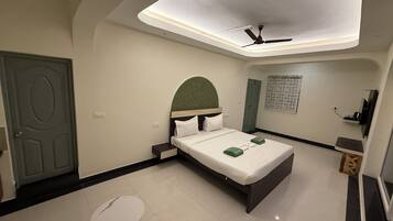 A hotel room with a bed, a ceiling fan, a small table, and a door.