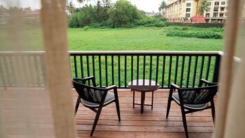 A balcony with two chairs and a small table, overlooking a grassy area with trees and a building in the background.
