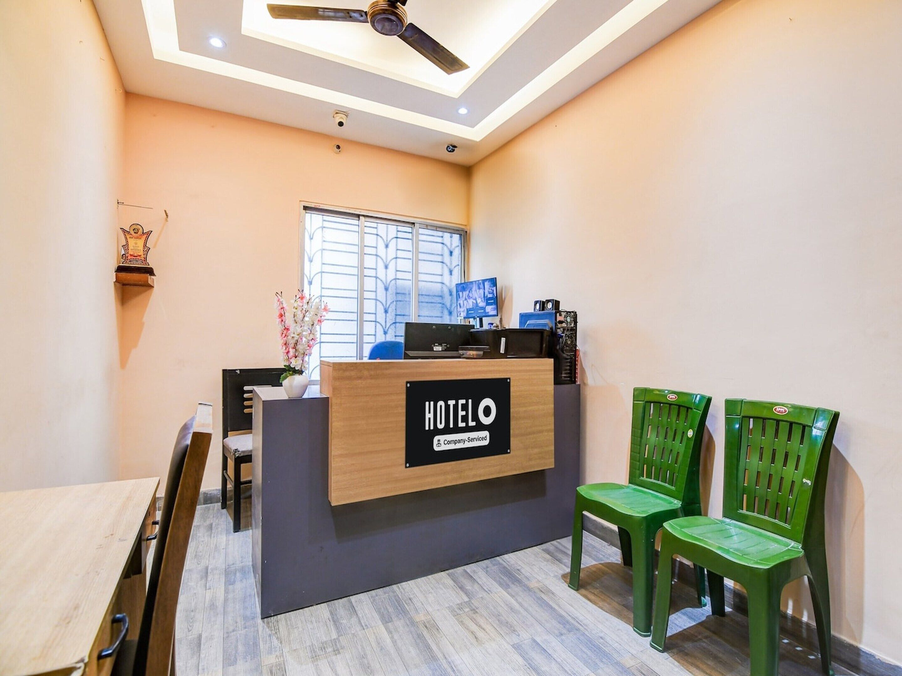 A hotel reception desk with a sign, a ceiling fan, and two green chairs.