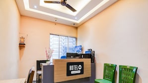 Un mostrador de recepción de hotel con un cartel, un ventilador de techo y dos sillas verdes.