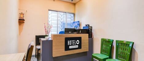 A hotel reception desk with a sign, a ceiling fan, and two green chairs.