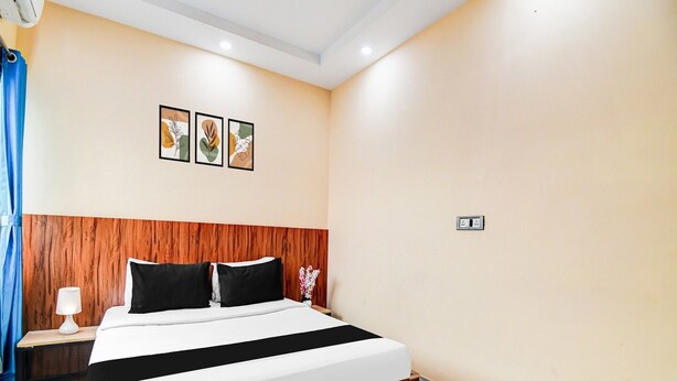 Habitación de hotel con cabecera de madera, cama con ropa de cama blanco y negro, mesita de noche con lámpara y un enchufe en la pared.