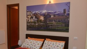 Una camera da letto con un letto, due cuscini, un comodino, una lampada e un quadro appeso al muro raffigurante un borgo.