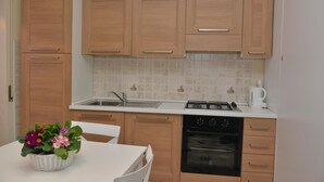 Una cucina con mobili in legno, un piano di lavoro bianco, un lavello, un fornello, un forno e un tavolo con una pianta in vaso.