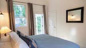 A bedroom with a bed, a nightstand, a lamp, a window with curtains, and a door. - BREATHTAKING : on water front with panoramic views + pool + dock (Dunmore Town)