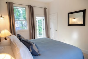 Ein Schlafzimmer mit einem Bett, einem Nachttisch, einer Lampe, einem Fenster mit Vorhängen und einer Tür.