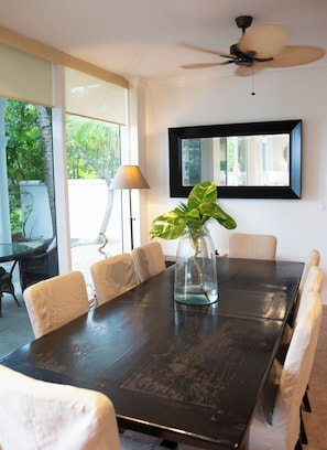 A dining area with a dark wooden table, white cushioned chairs, a glass vase with a plant, a ceiling fan, and a large window with a view of greenery. - BREATHTAKING : on water front with panoramic views + pool + dock (Dunmore Town)