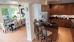 A modern kitchen with a central island, wooden cabinets, and a dining area with a table and chairs. - BREATHTAKING : on water front with panoramic views + pool + dock (Dunmore Town)