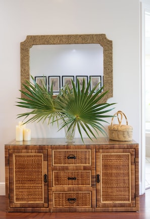 Ein Holzschrank mit Korbmöbel-Details, ein Spiegel und ein Blumentopf.