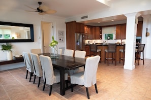 A dining area with a dark wooden table and chairs, a ceiling fan, and a kitchen in the background. - BREATHTAKING : on water front with panoramic views + pool + dock (Dunmore Town)