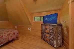 A bedroom with a bed, a dresser, a television, and a window. - Luxury Sevierville Mountain Cabin • Hot Tub • Game Room • Sleeps 12 (Sevierville)
