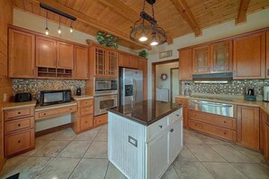 A kitchen with wooden cabinets, a central island, and a tiled backsplash. - Luxury Sevierville Mountain Cabin • Hot Tub • Game Room • Sleeps 12 (Sevierville)