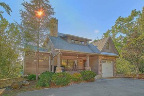 A two-story house with a covered porch, a garage, and a chimney. - Luxury Sevierville Mountain Cabin • Hot Tub • Game Room • Sleeps 12 (Sevierville)