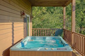 Un jacuzzi en una terraza de madera con barandilla, rodeado de árboles.