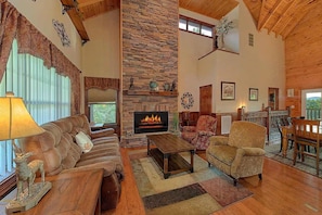 A cozy living room with a fireplace, leather sofa, and a dining area with wooden furniture. - Luxury Sevierville Mountain Cabin • Hot Tub • Game Room • Sleeps 12 (Sevierville)