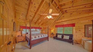 Ein Schlafzimmer in einer Blockhütte mit einem Himmelbett, einem Sofa und einem Deckenventilator.