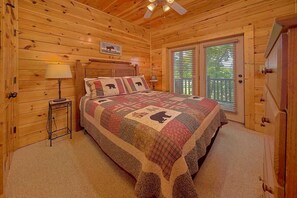 Ein Schlafzimmer einer Holzhütte mit einem Bett, einem Nachttisch, einer Lampe und einem Fenster mit Jalousien.
