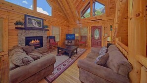 Ein rustikales Blockhaus im Inneren mit Kamin, Sofas, einem Fernseher und einem Deckenventilator.
