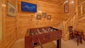 Ein Zimmer mit Holzboden, einem Fußballtisch, einem an der Wand montierten Fernseher und gerahmten Bildern.
