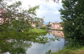 A calm river with a bridge, surrounded by greenery and buildings in the background.