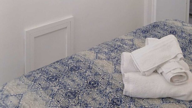 Une chambre avec un lit, un téléviseur à écran plat fixé au mur, une porte et une serviette sur le lit.