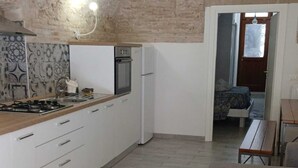 A kitchen with white cabinets, a stove, and a refrigerator. There is a wooden bench and a sofa in the living area.