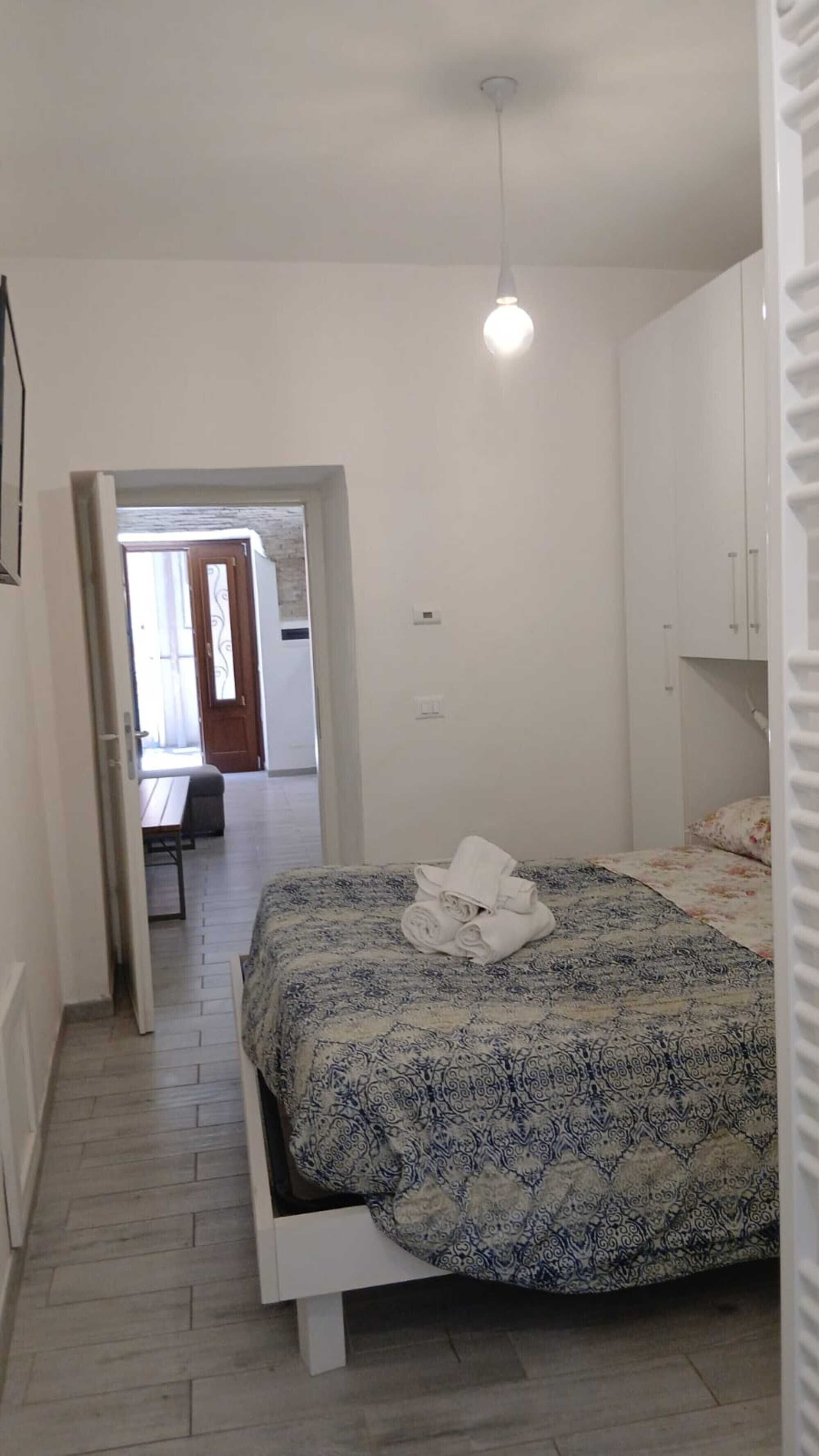 Une chambre à coucher comprenant un lit, une armoire, un luminaire suspendu et donnant sur une autre pièce.