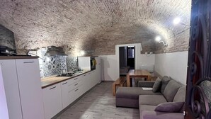 A modern interior with a stone ceiling, a kitchen area, a seating area with a sofa and ottoman, and a dining table.