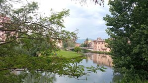 A calm river with a bridge, surrounded by greenery and buildings in the background.