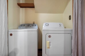Une buanderie équipée de deux machines à laver, une Whirlpool et une Amana, et d’une étagère en bois placée au-dessus.