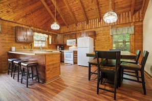 A wooden cabin interior with a kitchen, dining area, and bar stools. - Cozy Gatlinburg Cabin, Sleeps 10 , Hot Tub , Game Loft (Gatlinburg)