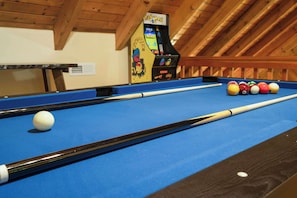A pool table with balls, a pool cue, and a video game machine in a room with wooden beams. - Cozy Gatlinburg Cabin, Sleeps 10 , Hot Tub , Game Loft (Gatlinburg)