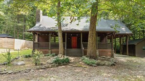A wooden cabin with a porch, surrounded by trees and a gravel path. - Cozy Gatlinburg Cabin, Sleeps 10 , Hot Tub , Game Loft (Gatlinburg)