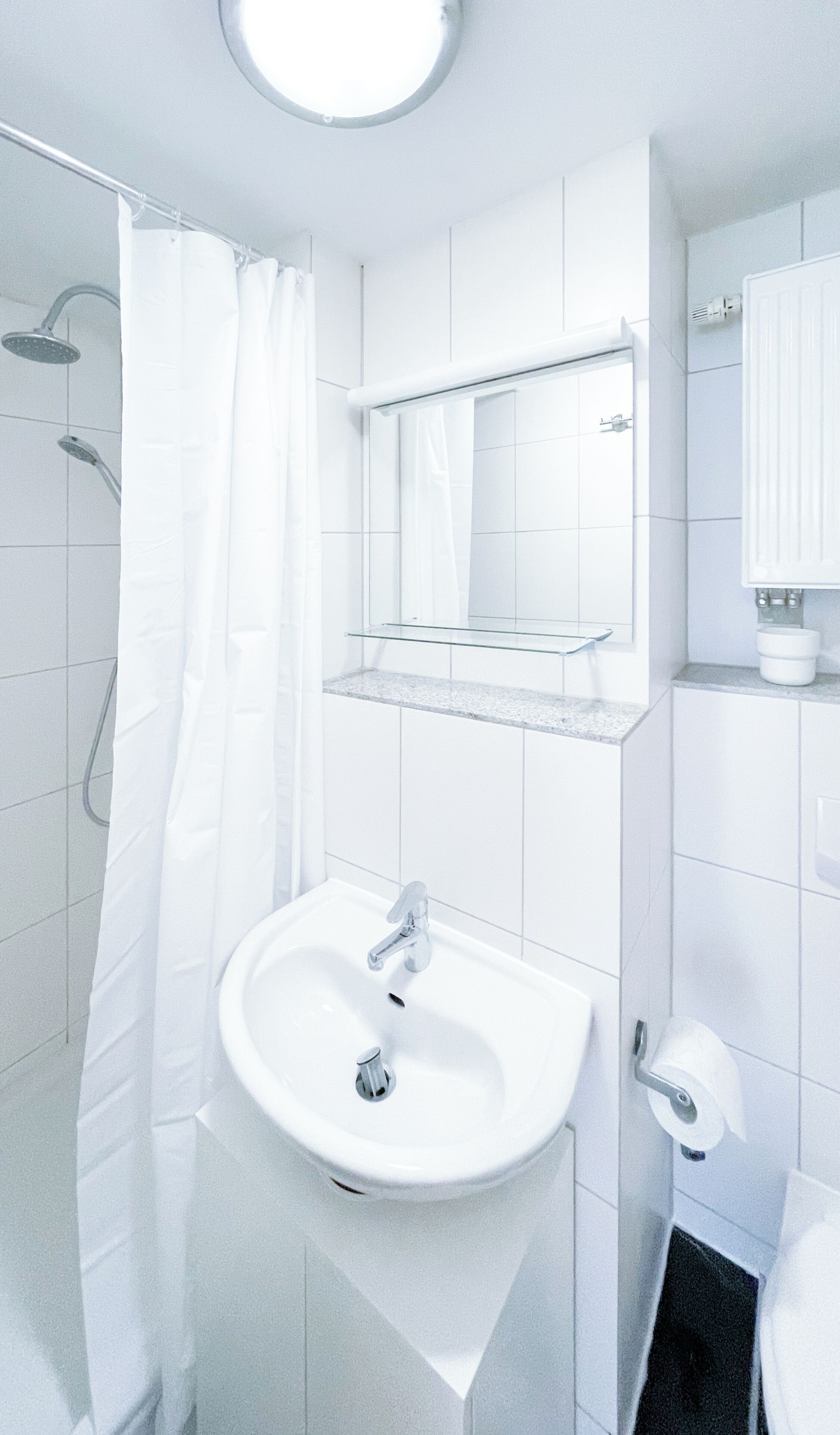 Een moderne badkamer met een wit wastafelmeubel, een glazen plank erboven, een douche met gordijn en een toilet met papierhouder.